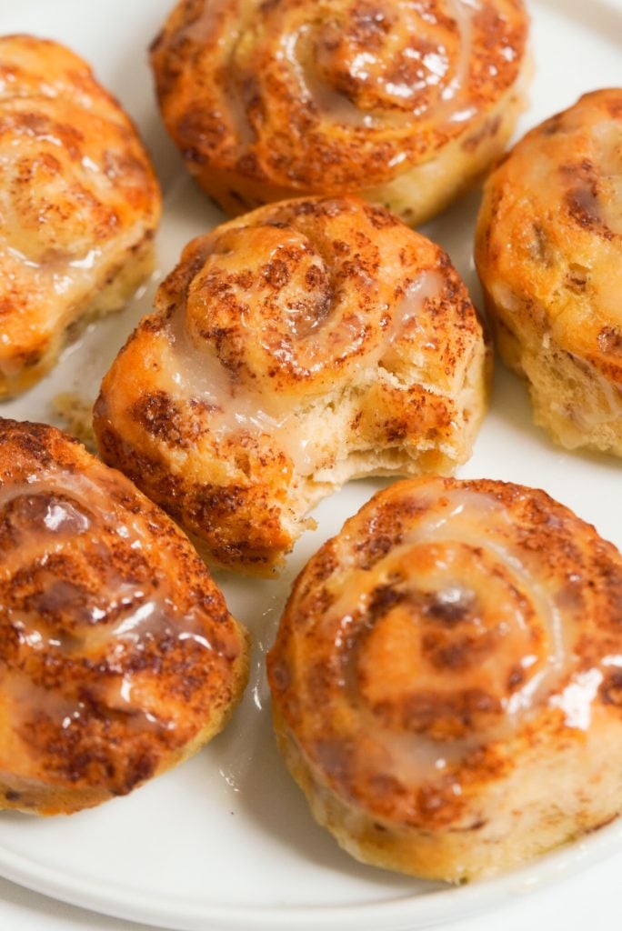 Air fryer cinnamon rolls on a white plate, one with a bite taken out in the middle