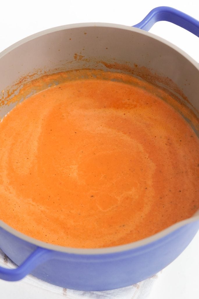 blue dutch oven filled with blended tomato soup with cream.