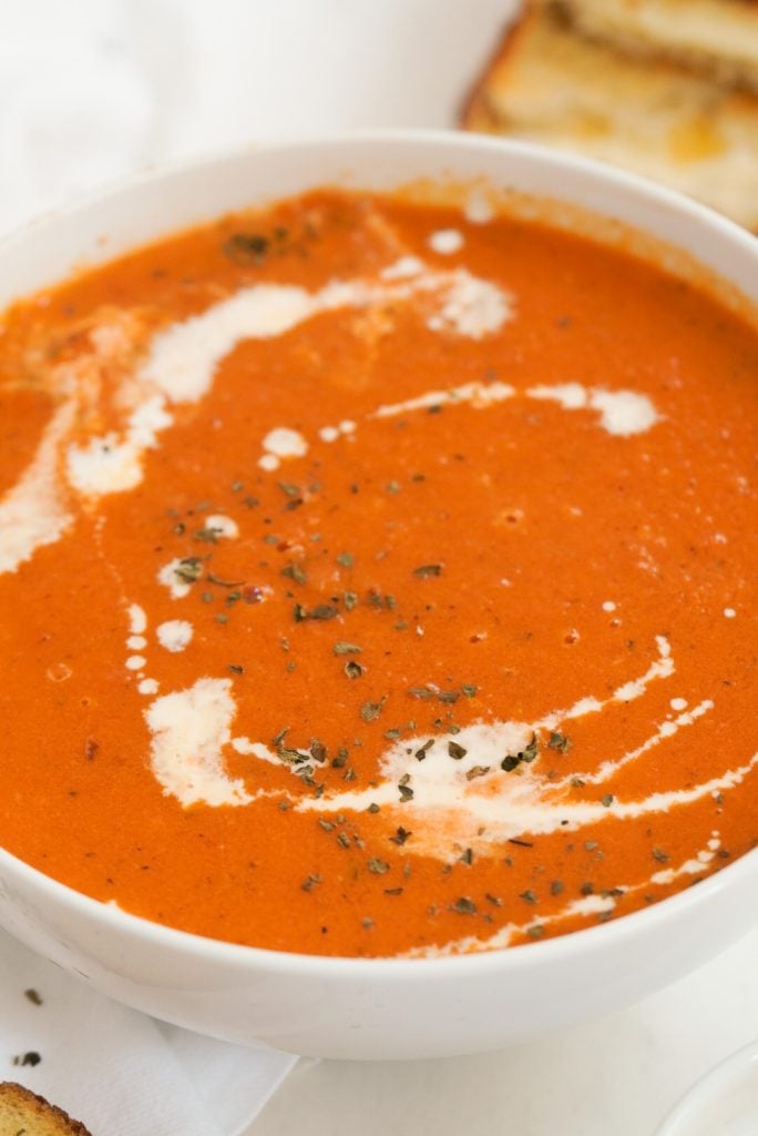 closeup shot of a bowl of tomato soup drizzled with a swirl of cream and topped with herbs.