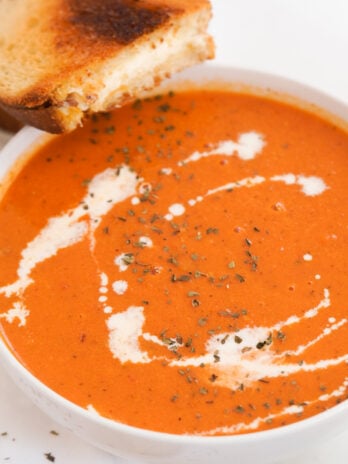 bowl of tomato soup with grilled cheese sandwich on the side.