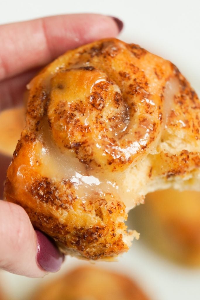 a hand holding an iced cinnamon roll made in the air fryer