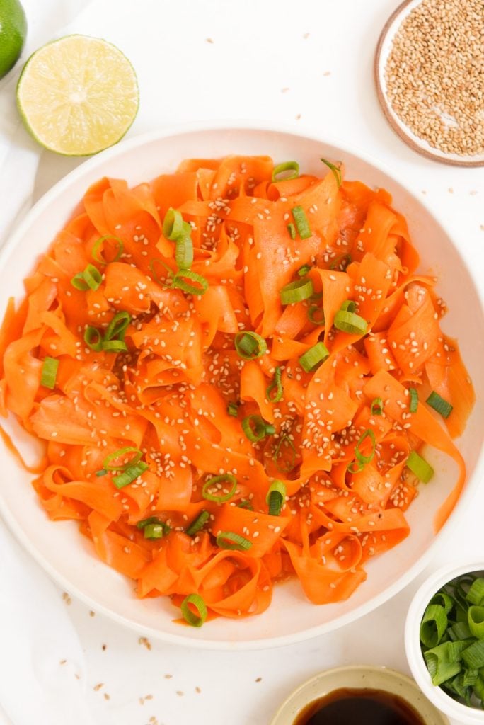 raw carrot salad on a plate with sesame seeds and green onions