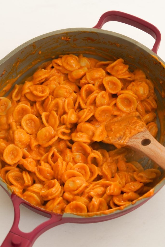 stirring cooked orecchette pasta into the spicy vodka sauce in the pan.