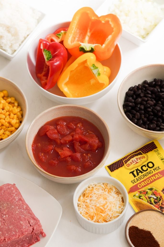 ingredients needed to make taco stuffed bell peppers measured out into bowls on a white table.