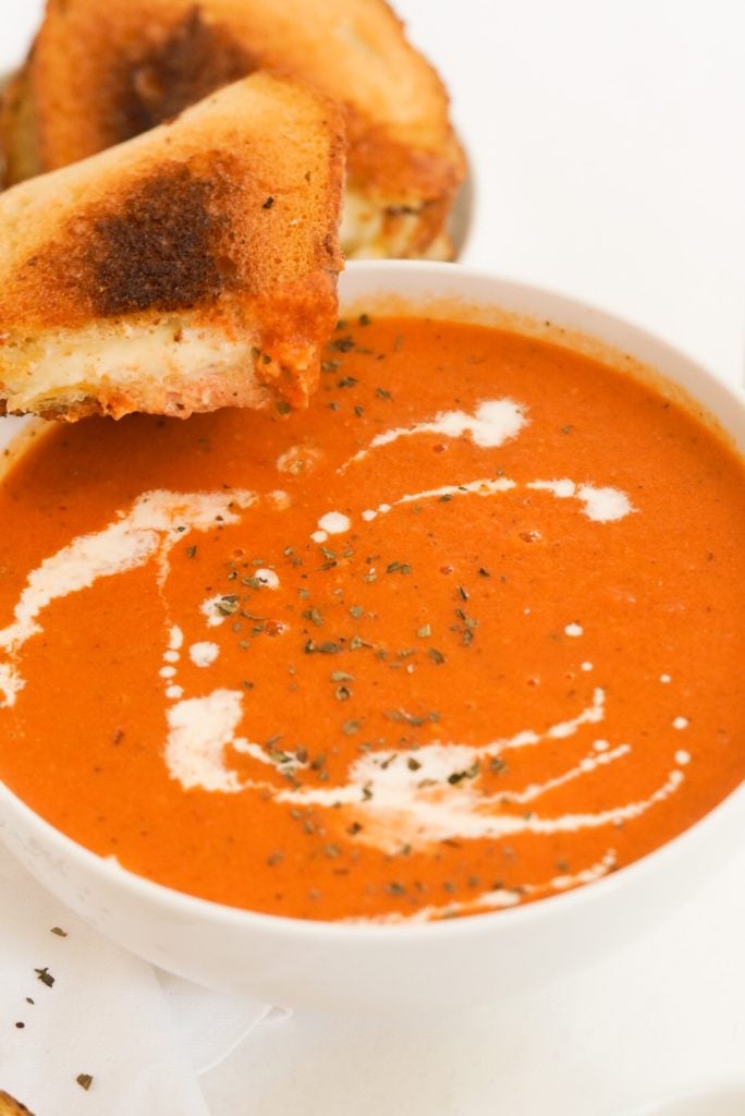 tomato soup with grilled cheese perched on the side of the bowl.