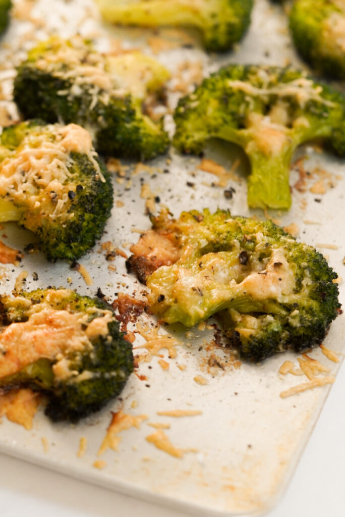 closeup shot of baked parmesan smashed broccoli florets on a baking sheet.