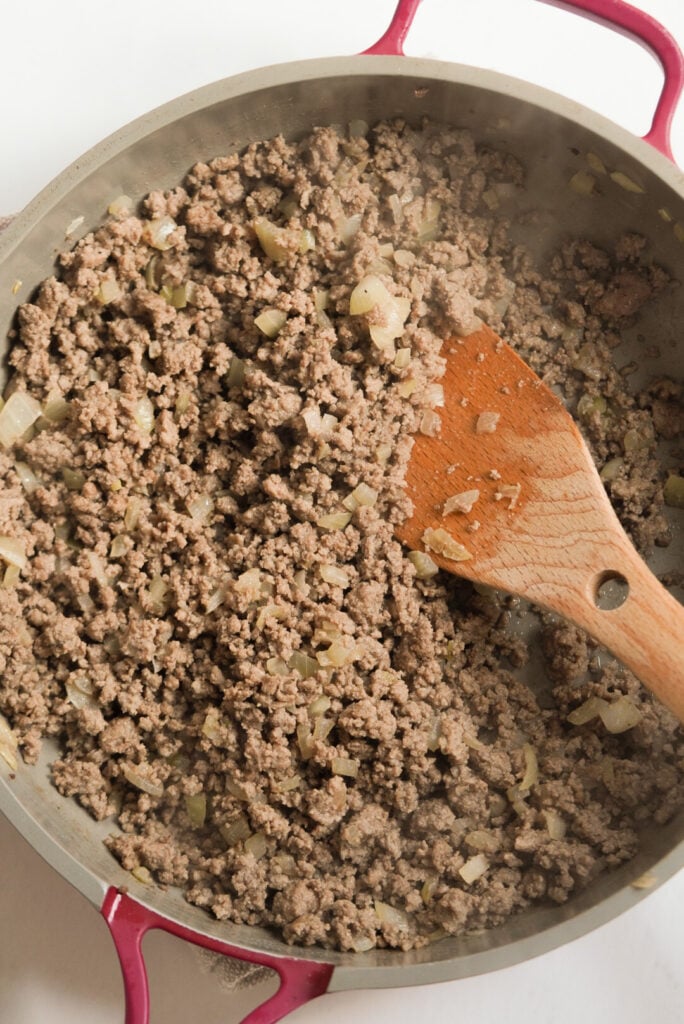 browned beef and potato chunks in a large skillet with a wooden spoon.