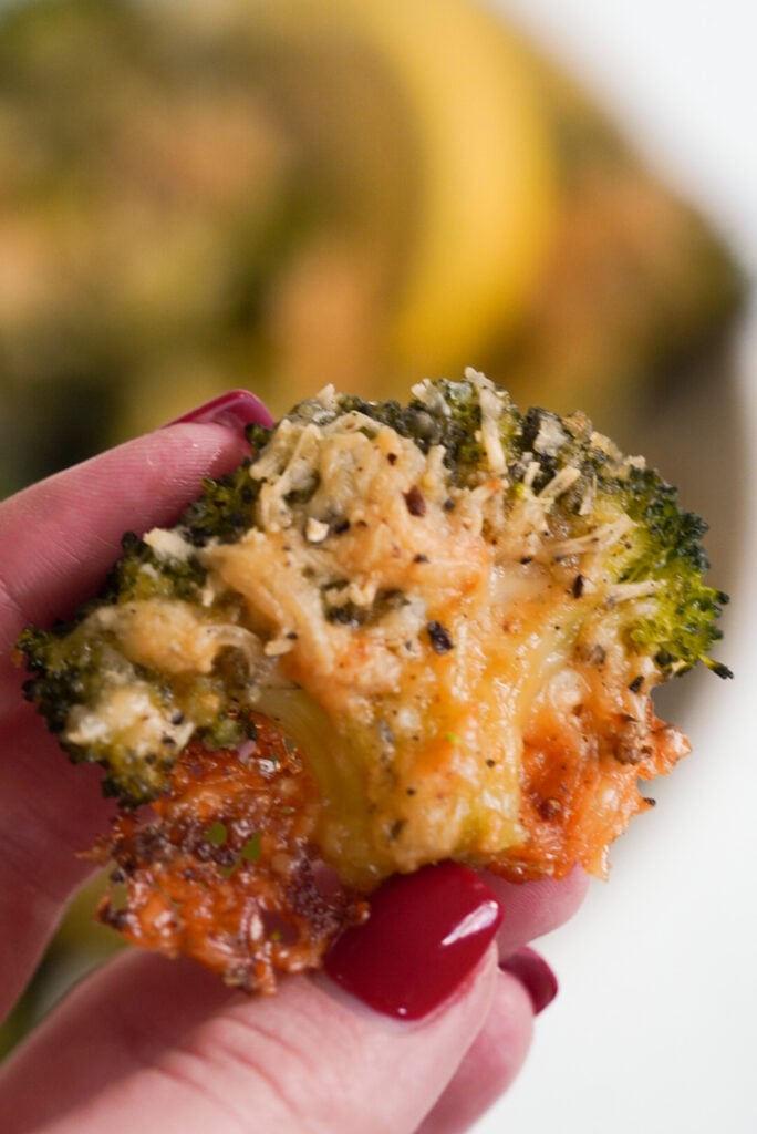 hand holding a floret of crispy, cheesy smashed broccoli parmesan.