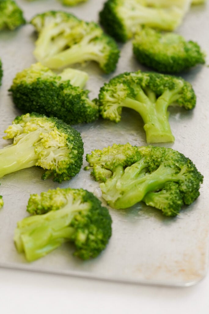 closeup on broccoli florets on a baking sheet after being smashed with a cup.