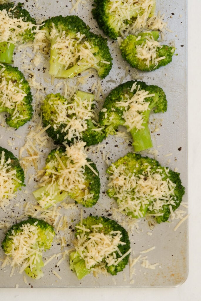 smashed broccoli with parmesan cheese shreds on a baking sheet prior to baking.