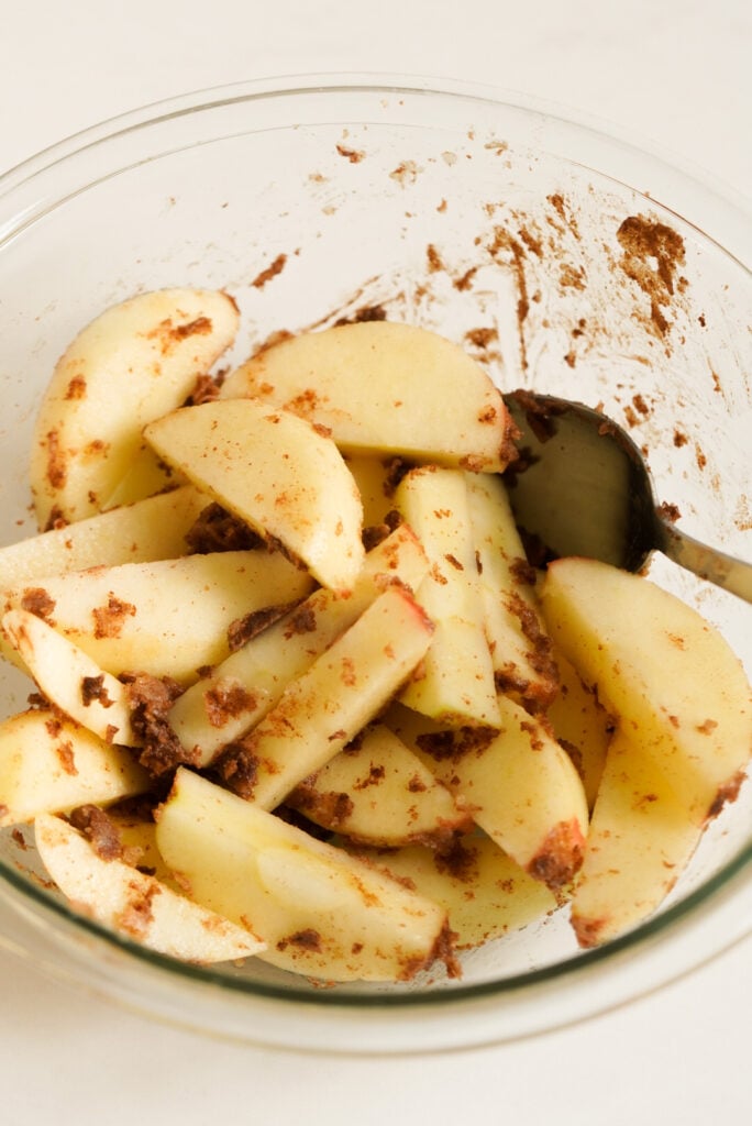 process shot of apple slices tossed with cinnamon sugar and melted butter in a mixing bowl.