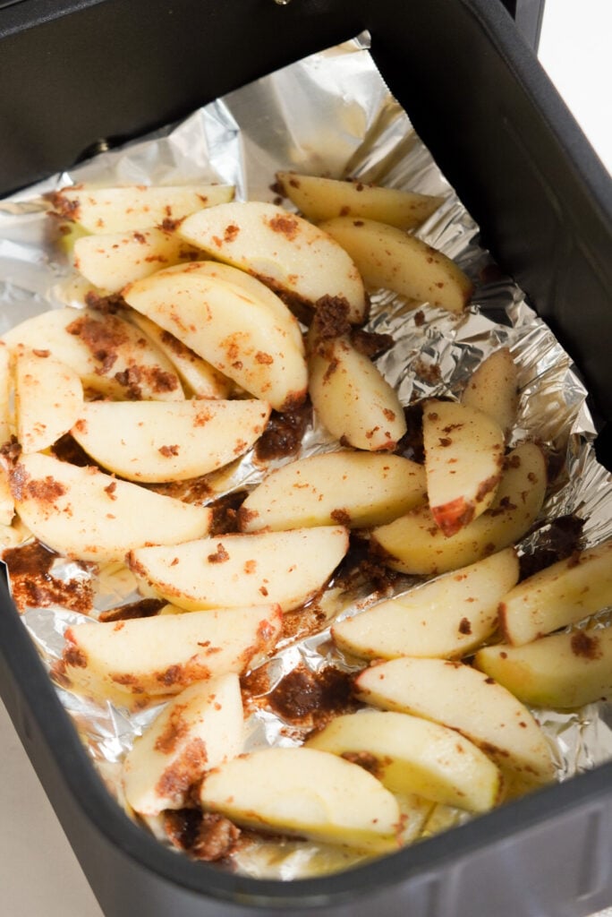 apples placed in the foil-lined basket of an air fryer before cooking.