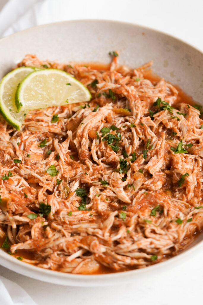 shredded salsa chicken in a bowl with fresh cilantro and lime