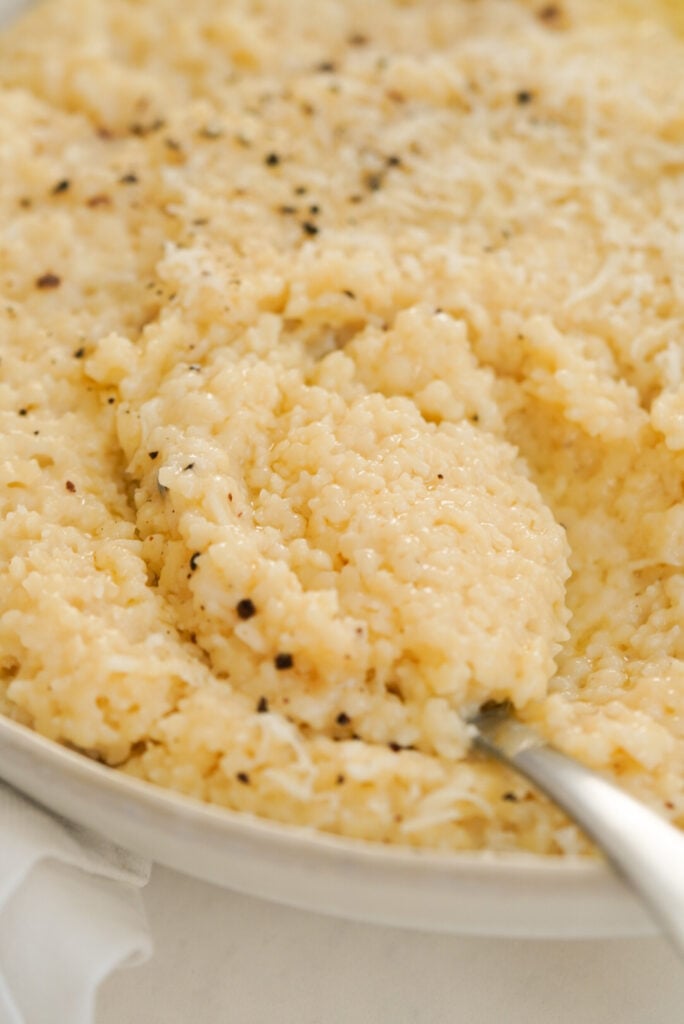 Spoon scooping pastina topped with parmesan cheese and black pepper