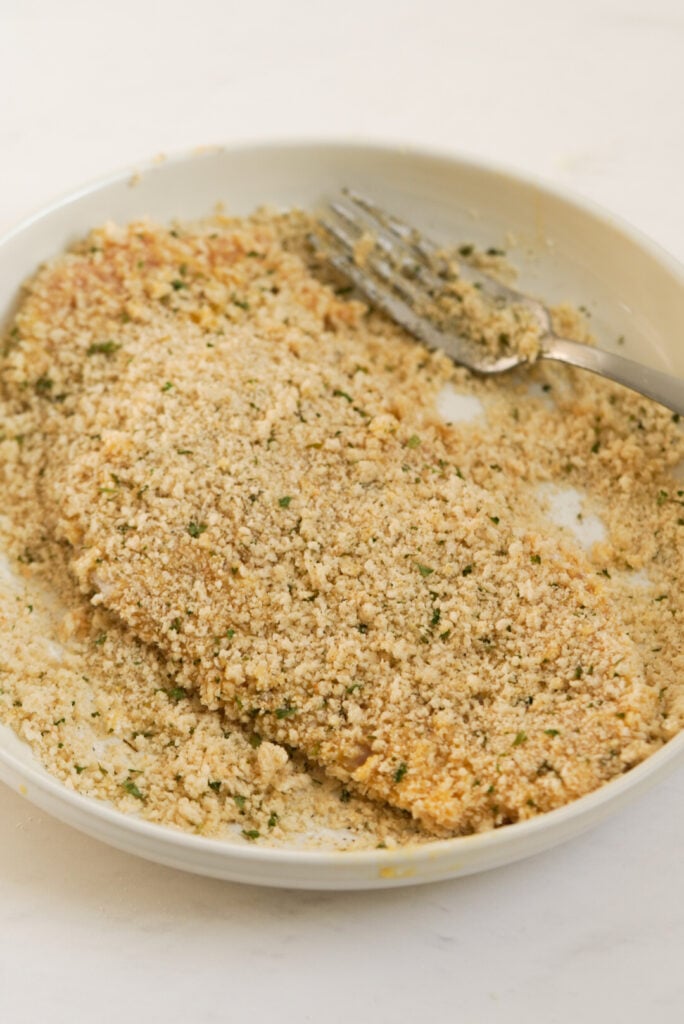 process shot - pounded chicken cutlet getting tossed in the breadcrumb mixture.