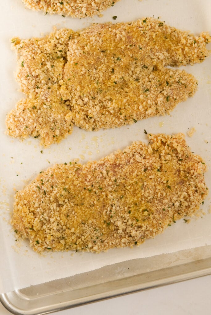 process shot - panko-breaded chicken cutlets on a baking sheet before baking.