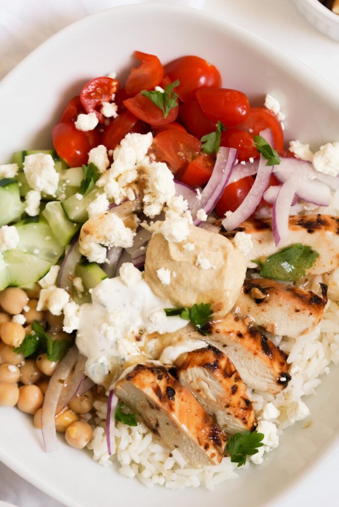 rice bowl with chicken, feta, tomatoes, cucumber, red onion, hummus, and tzatziki