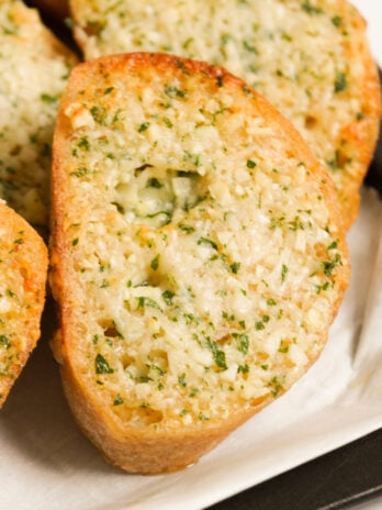 closeup shot of a slice of cheesy air fryer garlic bread on a white plate.