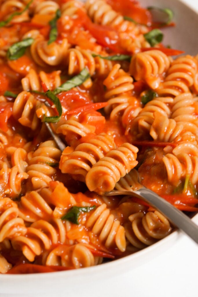 closeup shot of spaghetti sauce with cherry tomatoes on cooked rotini pasta.
