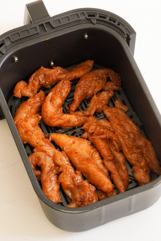 naked seasoned chicken tenderloins in the air fryer basket before cooking.
