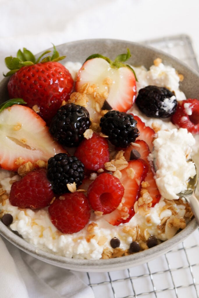 bowl of cottage cheese with fresh berries, honey, and granola on top