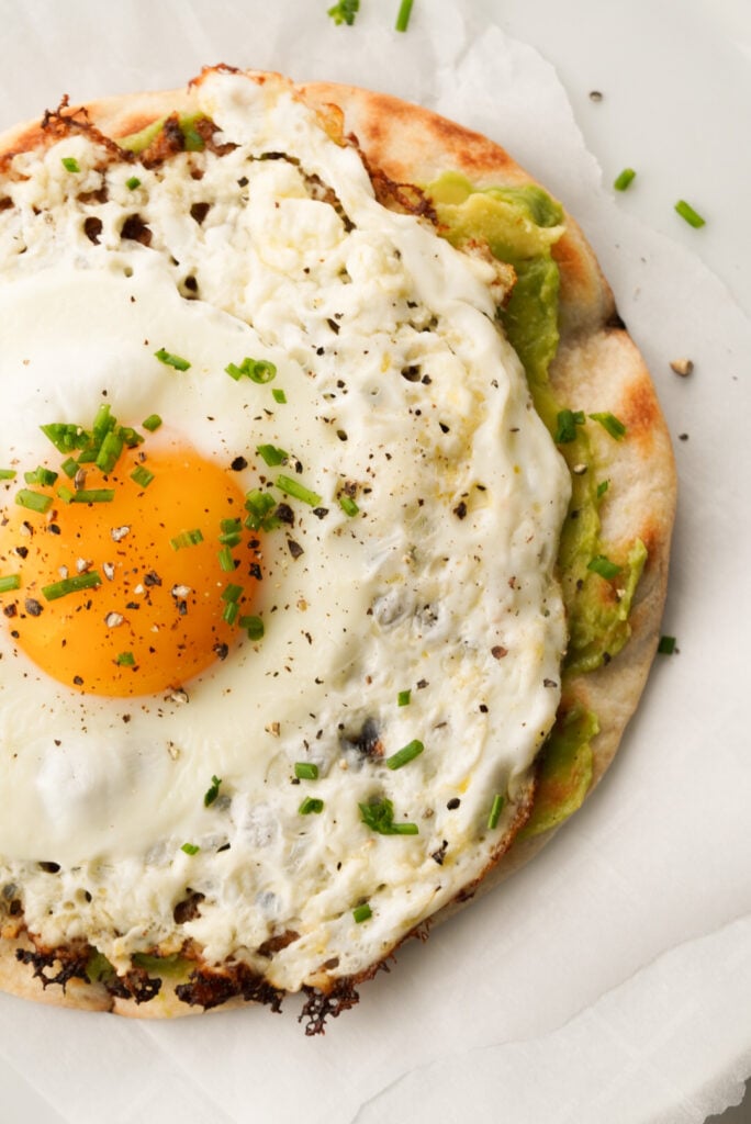a egg fried in feta cheese on a tortilla with avocado 