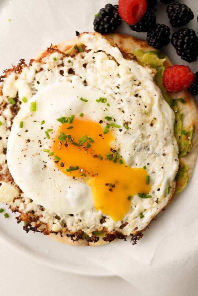 Feta cheese fried egg on top of a tortilla with avocado. Berries on the side.