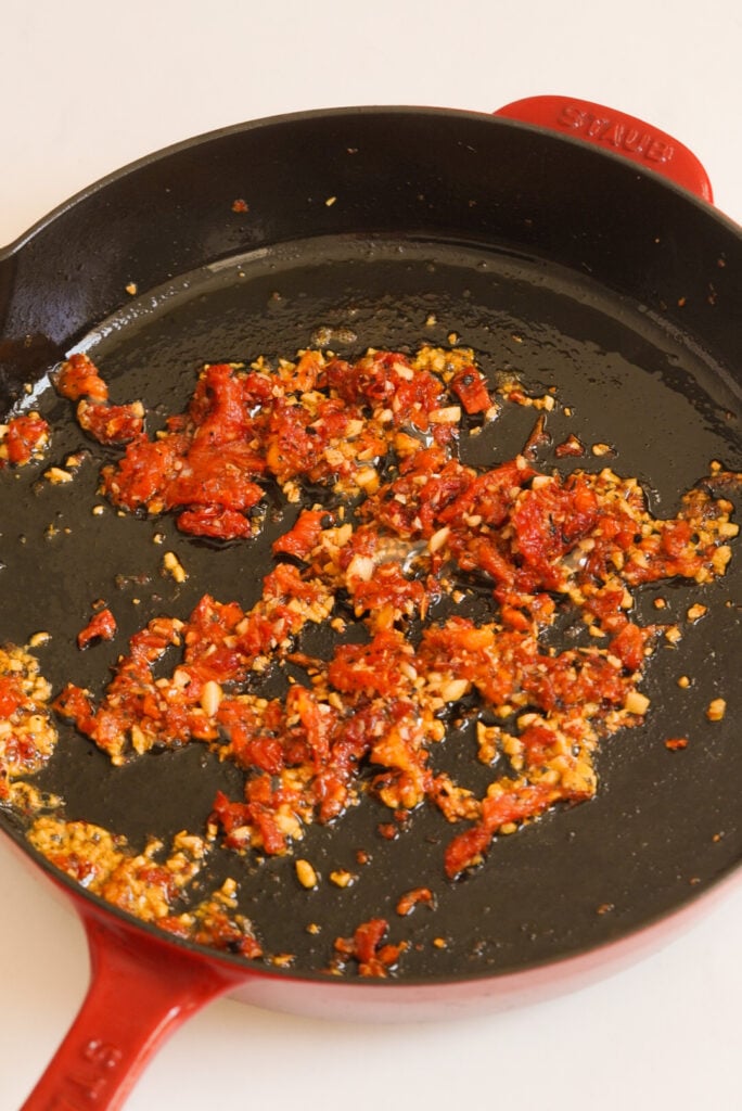 sun dried tomatoes and garlic sauteing in a red staub skillet.
