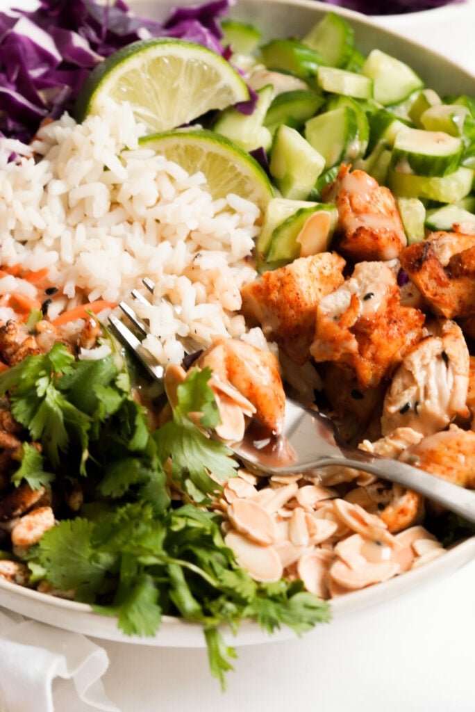 fork taking a bite of a rice bowl with chicken, lettuce, crispy rice, almonds, and fresh veggies