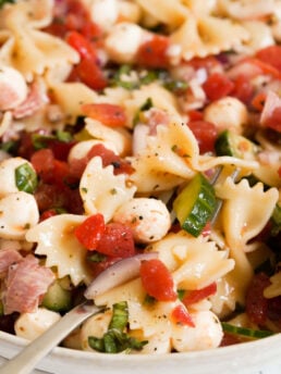 closeup on a forkful of Italian bow tie pasta salad in a white bowl.