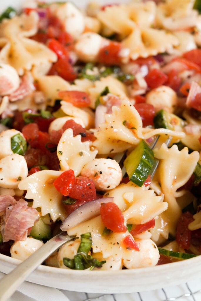 closeup on a forkful of Italian bow tie pasta salad in a white bowl.