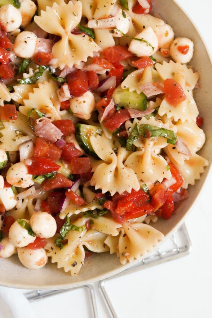 bowtie pasta salad with salami and italian dressing in a white bowl.