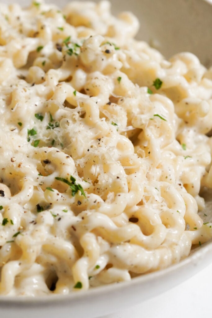 closeup shot of cottage cheese alfredo pasta topped with parmesan, parsley, and black pepper.