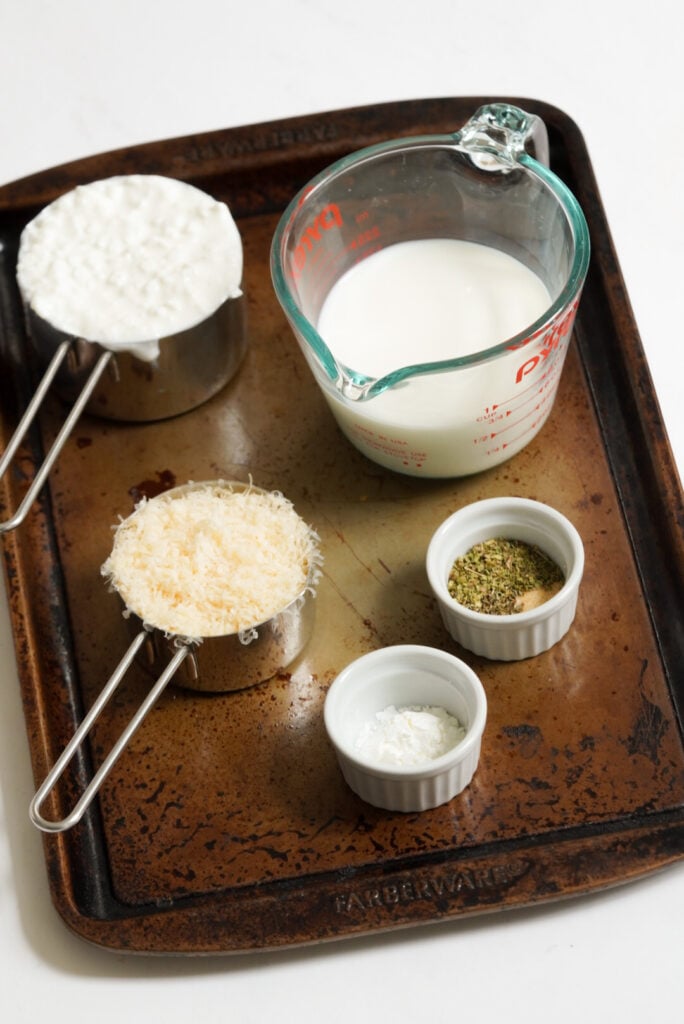 ingredients needed to make cottage cheese alfredo measured out into cups and bowls on a cookie sheet.