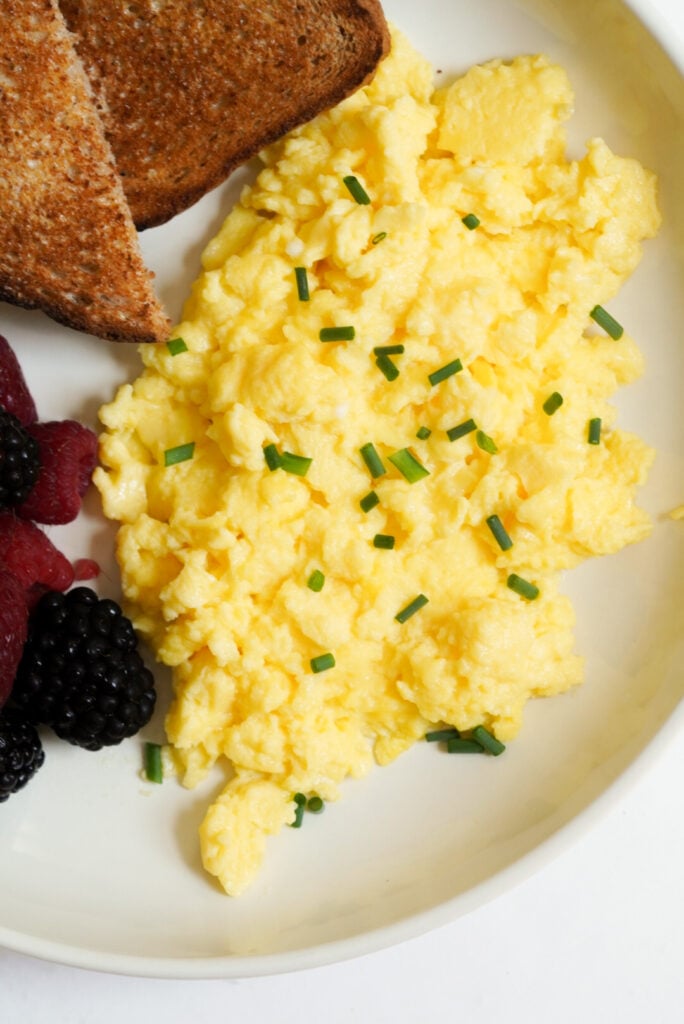 overhead shot of a breakfast plate with cottage cheese eggs, fresh blackberries and raspberries, and buttered wheat toast. 