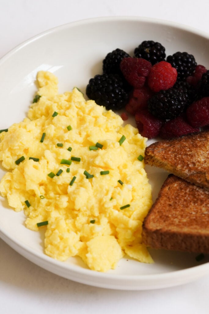 white pasta bowl with tender cottage cheese eggs, buttered toast, and a medley of fresh berries. 