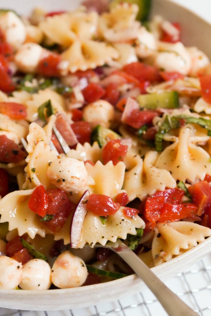 silver forkful of italian bowtie pasta salad with tomatoes and fresh mozzarella pearls.