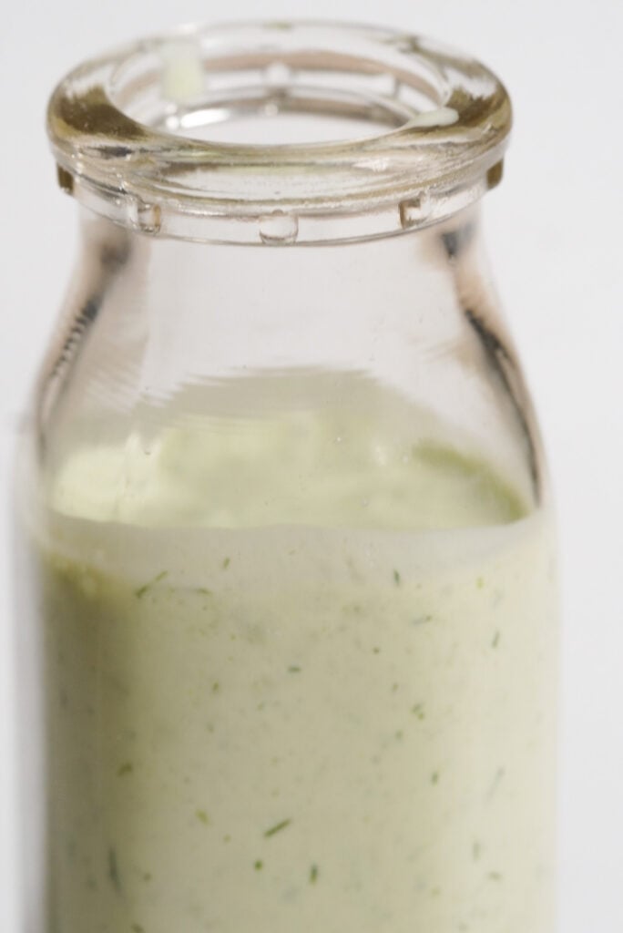 small glass milk jar filled with homemade healthy greek yogurt ranch dressing.