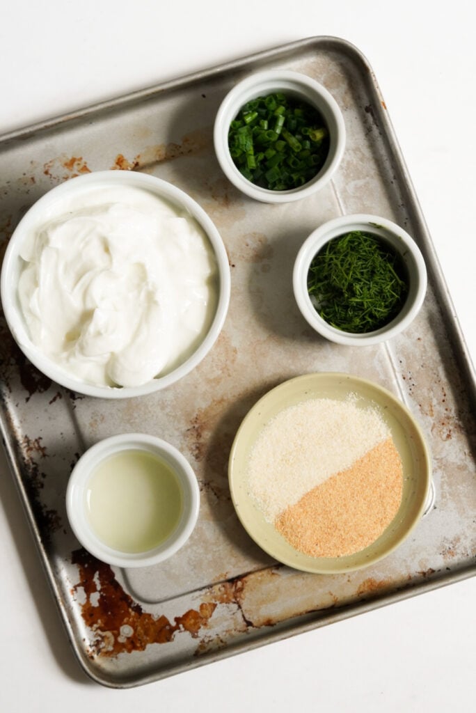 ingredients needed to make greek yogurt ranch measured out into white bowls on a stained silver cookie sheet.