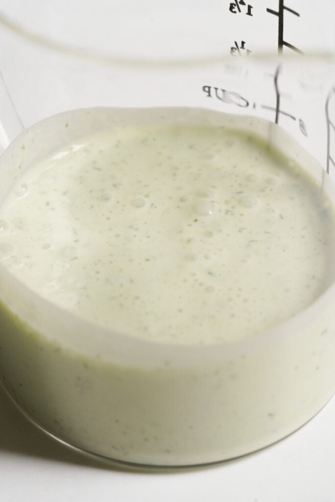 herby greek yogurt ranch dressing in a glass measuring beaker.