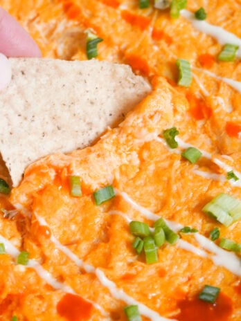 hand dunking a tortilla chip into healthy buffalo chicken dip.