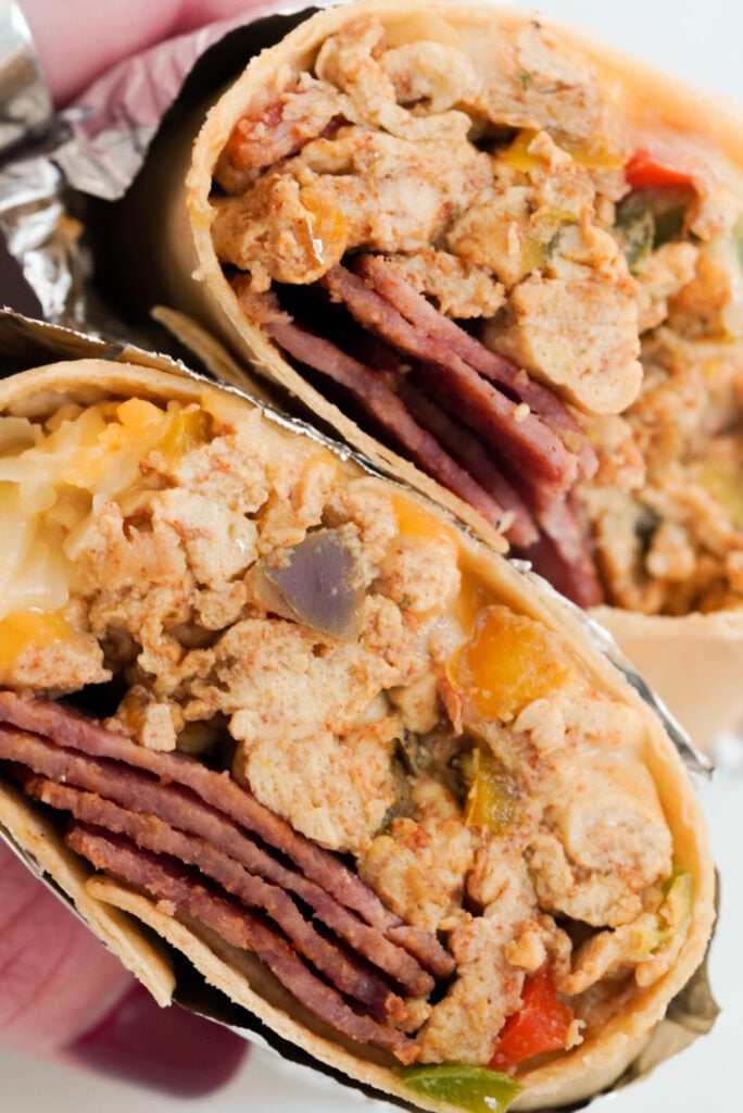 hand with maroon nail polish holding a bacon and egg high protein breakfast burrito.