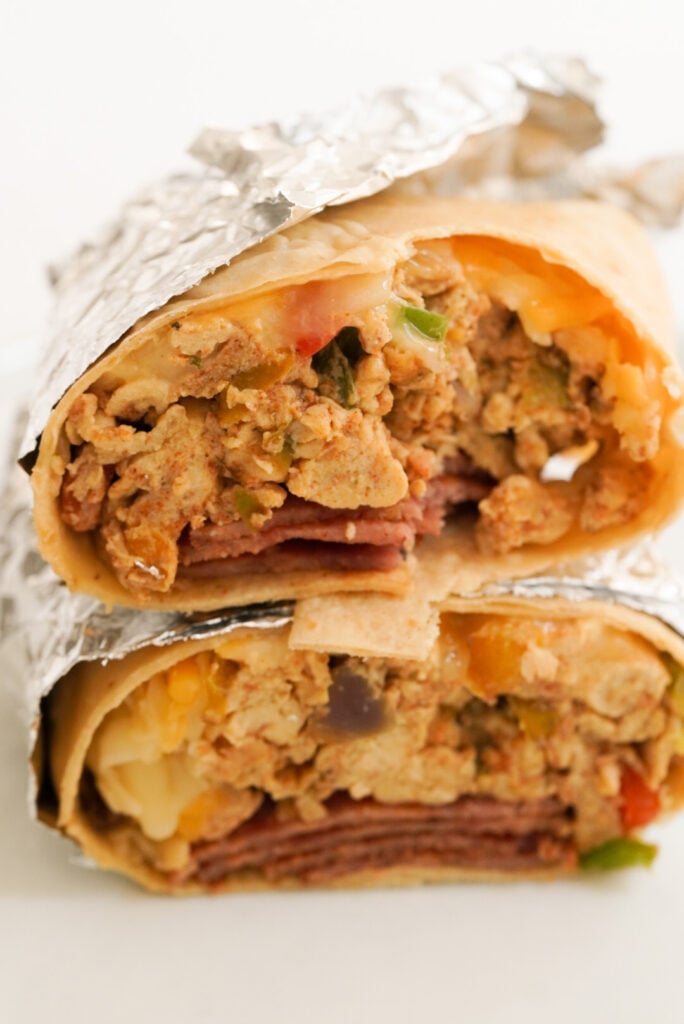 side on view of a stacked high protein breakfast burrito on a white table.