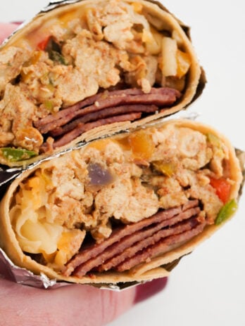 hand holding a foil-wrapped breakfast burrito filled with high-protein ingredients like eggs, egg whites, cheese, and turkey bacon.