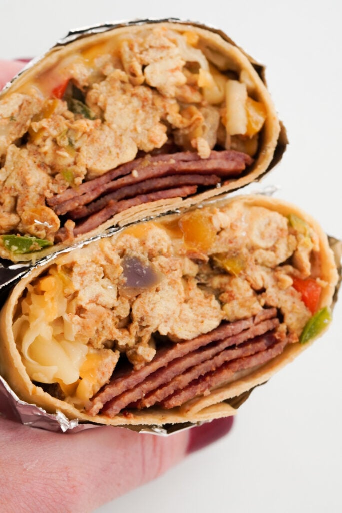 hand holding a foil-wrapped breakfast burrito filled with high-protein ingredients like eggs, egg whites, cheese, and turkey bacon.