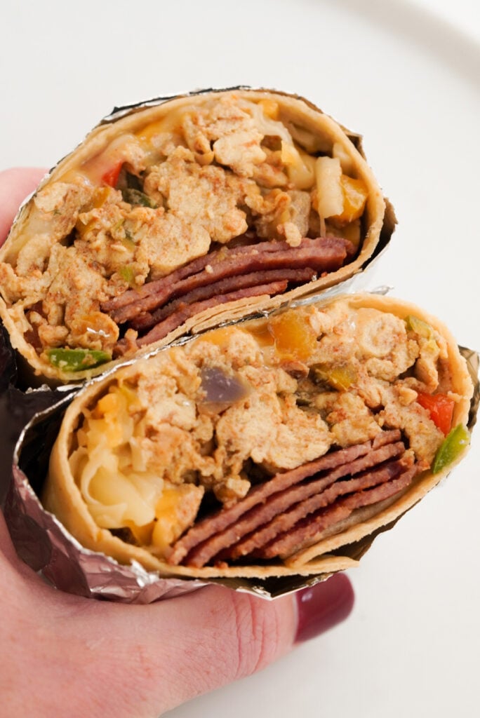 hand holding a bacon egg and cheese breakfast burrito that has been wrapped in foil and cut in half to show the insides.