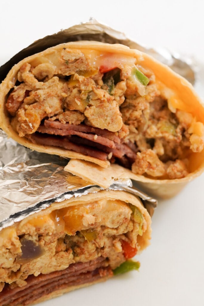 two halves of a foil wrapped high protein breakfast burrito stacked on top of each other on a white table.