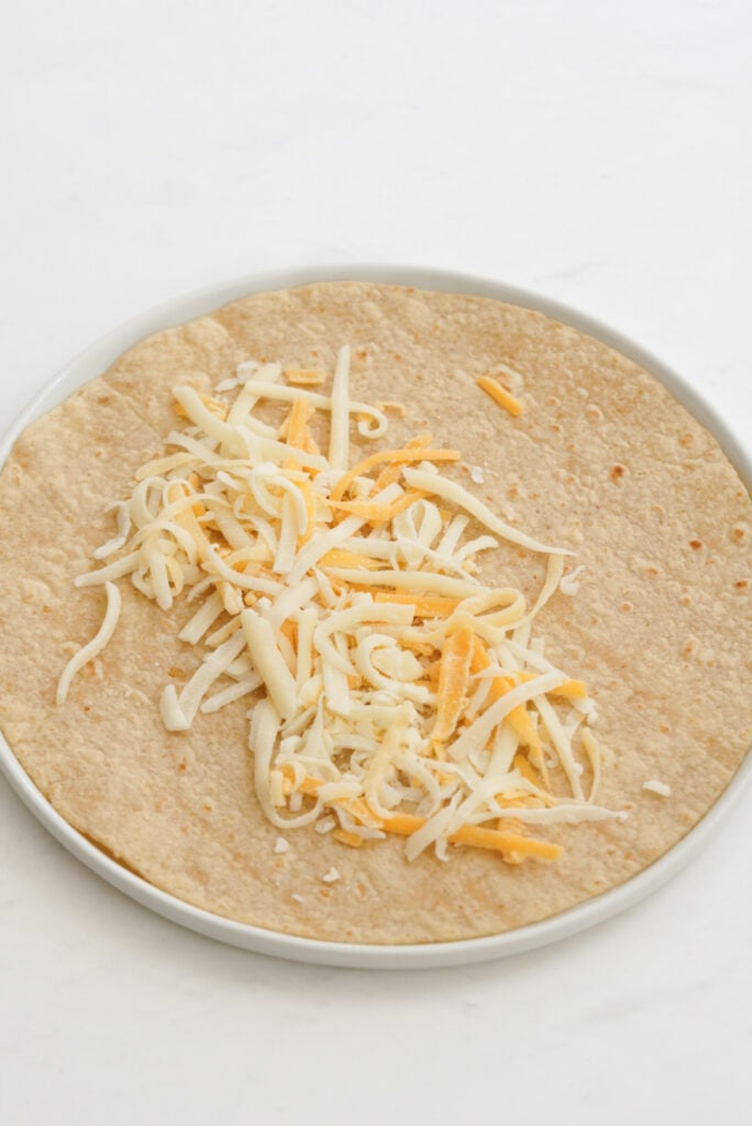 open faced tortilla with a layer of two colors of shredded cheese down the middle.