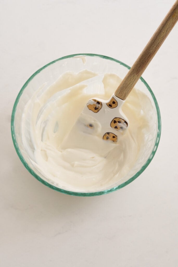 clear bowl with the mixed greek yogurt fruit dip and a wooden-handled spatula with a white silicone head adorned by cartoon chocolate chip cookies.