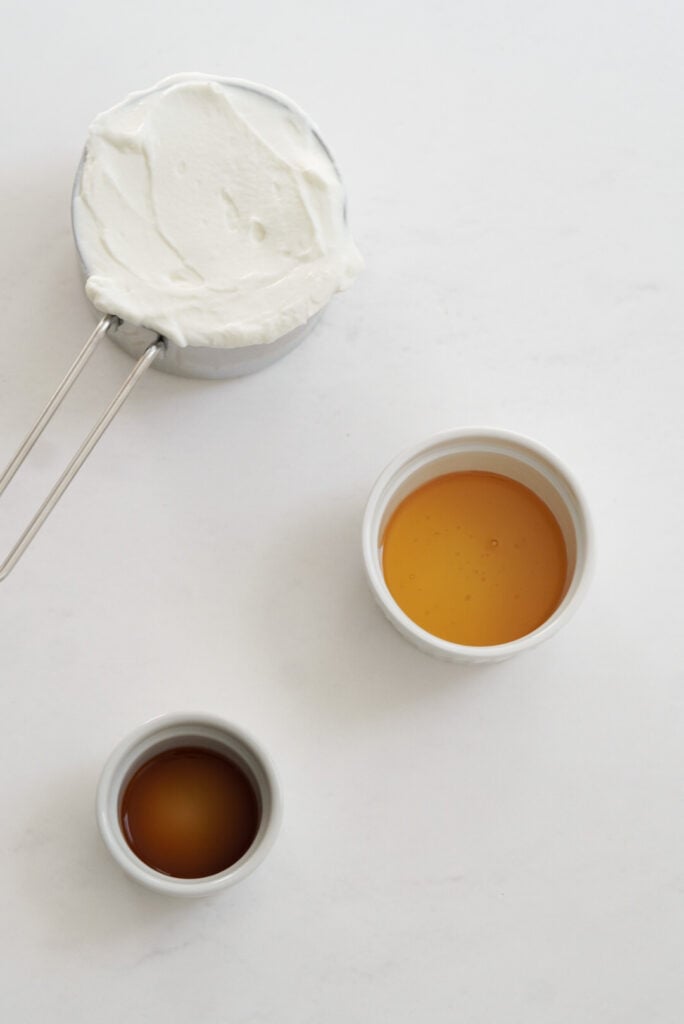 greek yogurt, honey, and vanilla extract measured out on a white table for making greek yogurt fruit dip recipe.